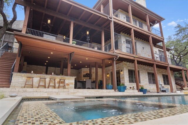 4403 Elohi Dr, Austin, TX 78746 - rear view of property featuring a balcony, stone siding, an outdoor pool, a patio area, and a hot tub