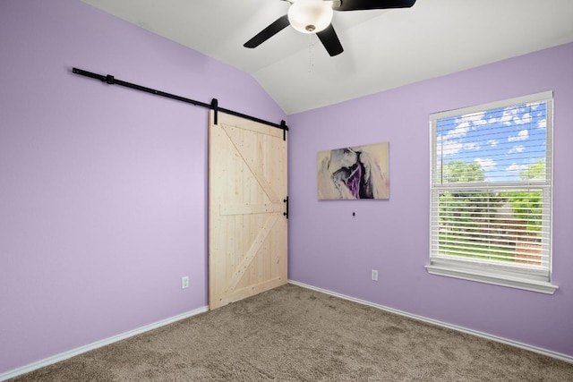 unfurnished bedroom featuring a ceiling fan, a barn door, carpet, baseboards, and vaulted ceiling