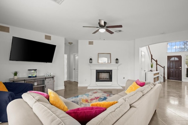 living area featuring stairway, ceiling fan, a fireplace with raised hearth, and visible vents