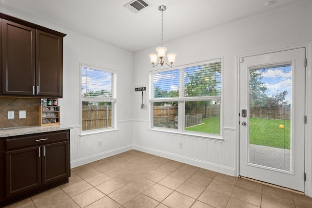 unfurnished dining area featuring a wainscoted wall, visible vents, a chandelier, light tile patterned floors, and baseboards