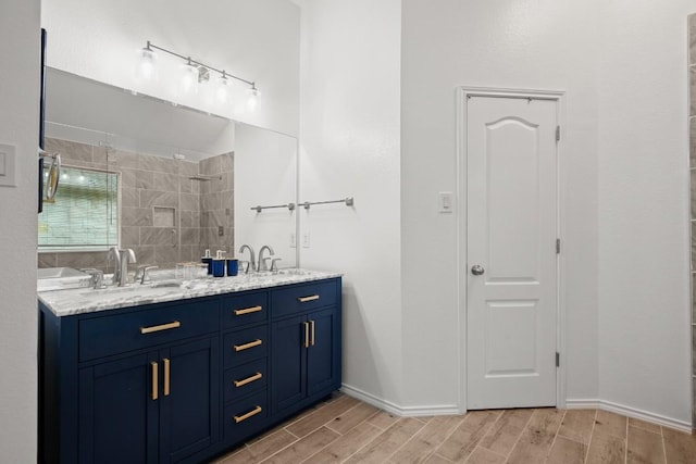 bathroom featuring double vanity, tiled shower, wood tiled floor, and a sink