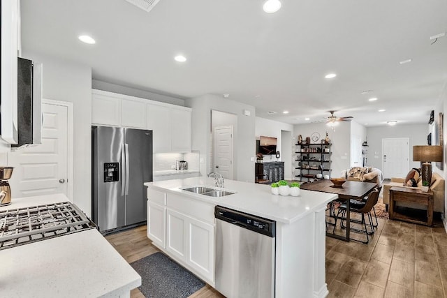 kitchen with light wood finished floors, a sink, open floor plan, appliances with stainless steel finishes, and light countertops
