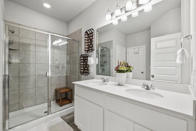 full bath with double vanity, a stall shower, wood finished floors, and a sink