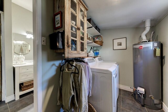 clothes washing area featuring water heater, independent washer and dryer, dark tile patterned floors, and baseboards