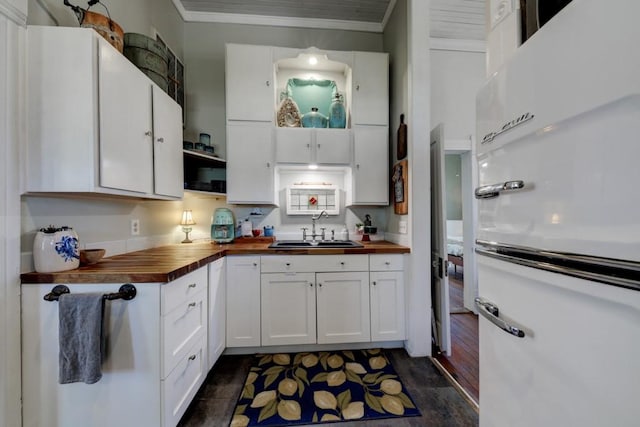 kitchen featuring wood counters, a sink, crown molding, white cabinets, and refrigerator