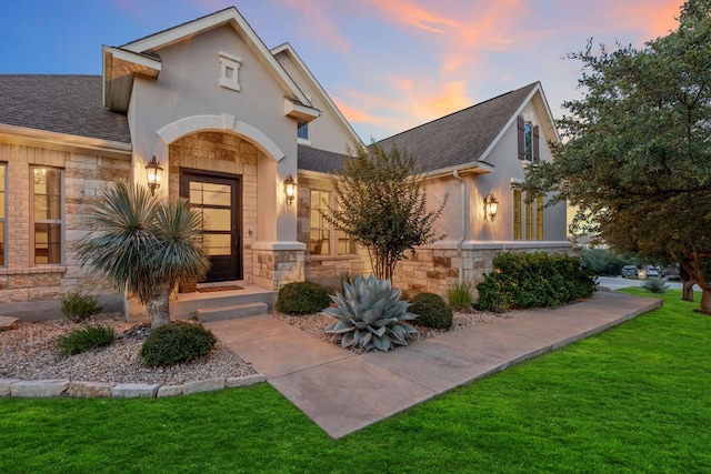 9525 Stratus Dr, Dripping Springs, TX 78620 - view of front facade with stone siding, a yard, a shingled roof, and stucco siding