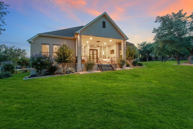 9525 Stratus Dr, Dripping Springs, TX 78620 - back of house at dusk with a lawn, ceiling fan, brick siding, and french doors