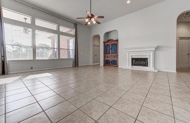 120 Mountain Laurel Way, Austin, TX 78737 - unfurnished living room featuring arched walkways, light tile patterned flooring, a ceiling fan, a fireplace with raised hearth, and baseboards