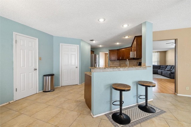 2103 Heather Dr, Cedar Park, TX 78613 - kitchen with freestanding refrigerator, a peninsula, a breakfast bar, light tile patterned floors, and light stone countertops