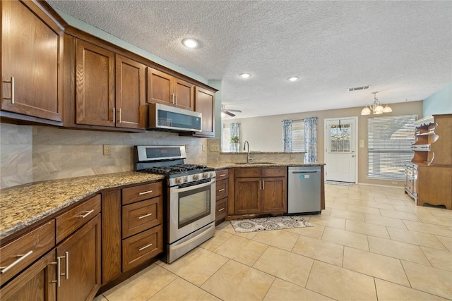 2103 Heather Dr, Cedar Park, TX 78613 - kitchen with appliances with stainless steel finishes, a peninsula, tasteful backsplash, a textured ceiling, and light stone counters