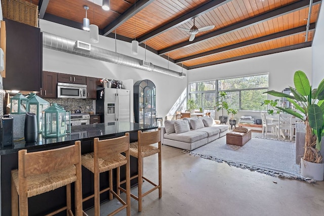 interior space featuring concrete flooring, beam ceiling, dark brown cabinetry, a breakfast bar, and appliances with stainless steel finishes