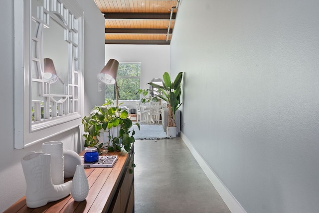 hall featuring beamed ceiling, baseboards, concrete floors, and wood ceiling