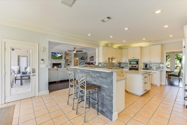 14415 Echo Blf, Austin, TX 78737 - kitchen featuring light tile patterned floors, a ceiling fan, a breakfast bar area, a warm lit fireplace, and crown molding