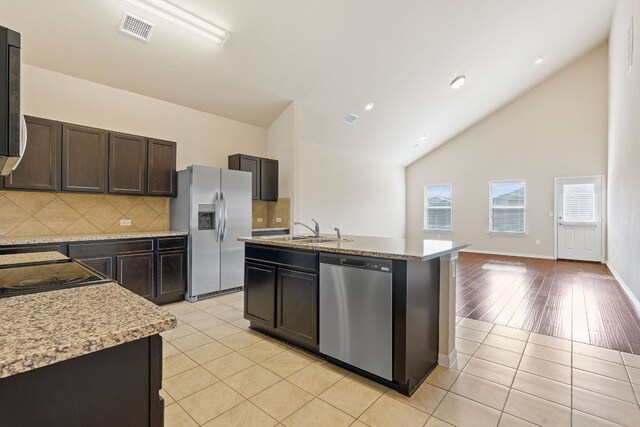 5825 Roderick Dr, Austin, TX 78724 - kitchen featuring appliances with stainless steel finishes, a sink, tasteful backsplash, a center island with sink, and light tile patterned floors