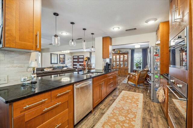 2402 Stevens Cv, Austin, TX 78723 - kitchen featuring stainless steel appliances, brown cabinetry, dark wood-type flooring, backsplash, and a textured ceiling