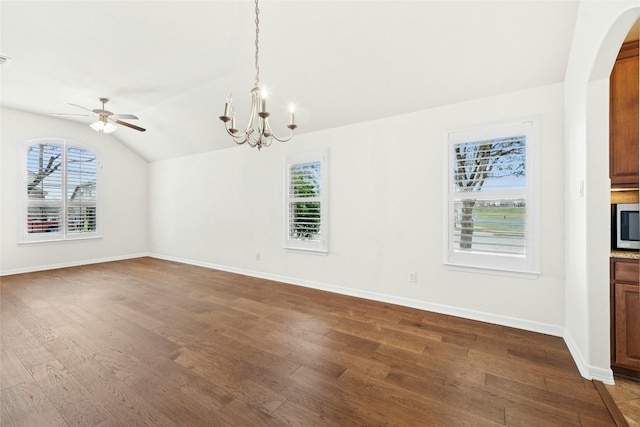 unfurnished dining area featuring arched walkways, baseboards, lofted ceiling, ceiling fan with notable chandelier, and dark wood-type flooring