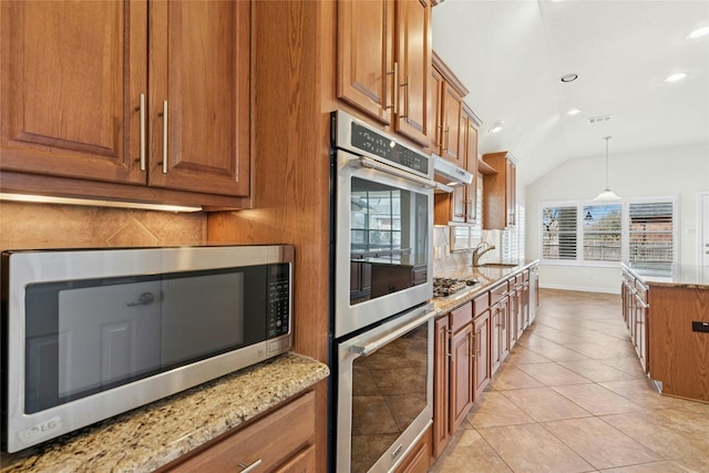 kitchen with brown cabinetry, light stone counters, a sink, and appliances with stainless steel finishes