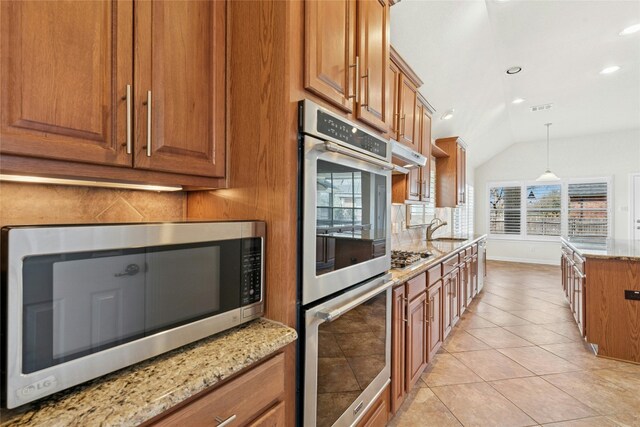 20700 Windmill Ridge St, Pflugerville, TX 78660 - kitchen with stainless steel appliances, brown cabinetry, a sink, light stone countertops, and lofted ceiling