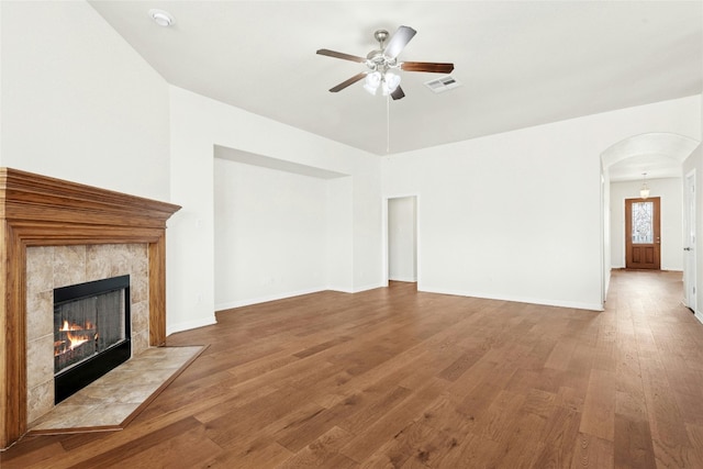 20700 Windmill Ridge St, Pflugerville, TX 78660 - unfurnished living room featuring a ceiling fan, arched walkways, a tiled fireplace, wood finished floors, and baseboards