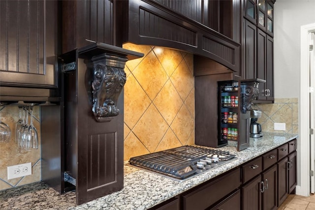 362 Wellington Dr, Austin, TX 78737 - kitchen featuring stainless steel gas cooktop, dark brown cabinetry, light stone countertops, glass insert cabinets, and tasteful backsplash