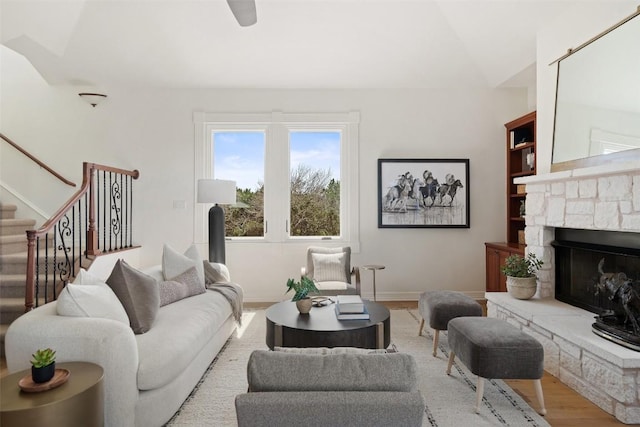 living area featuring baseboards, lofted ceiling, wood finished floors, stairway, and a fireplace