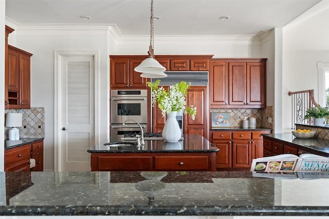 kitchen featuring a sink, decorative backsplash, double oven, a center island with sink, and decorative light fixtures