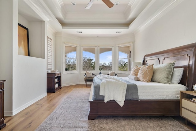 bedroom with light wood finished floors, a tray ceiling, ornamental molding, and multiple windows