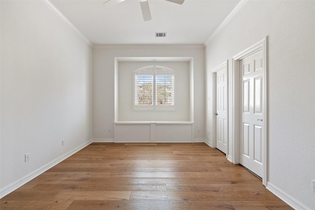 empty room with a ceiling fan, wood finished floors, baseboards, ornamental molding, and visible vents