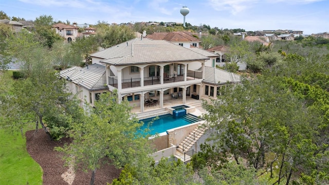 rear view of property featuring a tiled roof, a balcony, a pool with connected hot tub, a patio, and stucco siding
