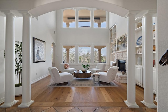 living room featuring tile patterned floors, a stone fireplace, baseboards, decorative columns, and built in features