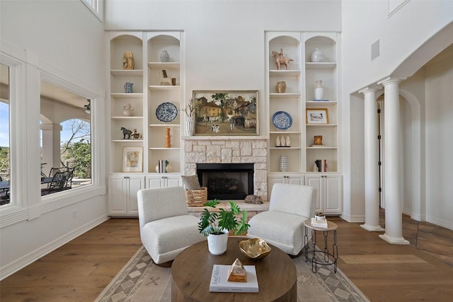 living room with baseboards, wood finished floors, a stone fireplace, and ornate columns