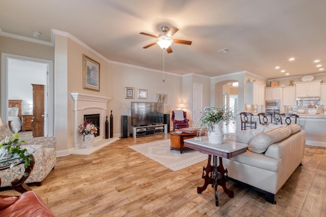 3204 Venezia Vw, Leander, TX 78641 - living room with a ceiling fan, light wood-style flooring, a fireplace with raised hearth, ornamental molding, and arched walkways