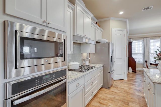 3204 Venezia Vw, Leander, TX 78641 - kitchen featuring appliances with stainless steel finishes, crown molding, light wood-type flooring, white cabinets, and light stone counters
