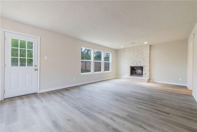 3901 Skipton Dr, Austin, TX 78727 - unfurnished living room with healthy amount of natural light, wood finished floors, a textured ceiling, a stone fireplace, and recessed lighting