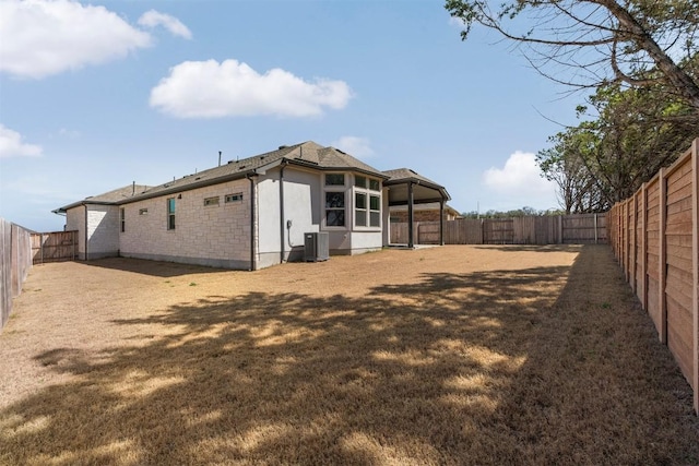 129 Du Bois Ln, Kyle, TX 78640 - back of property featuring a fenced backyard, stucco siding, central air condition unit, and stone siding