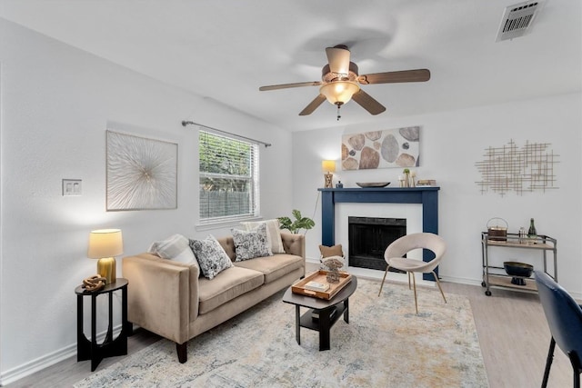 living room with wood finished floors, ceiling fan, a fireplace, and baseboards