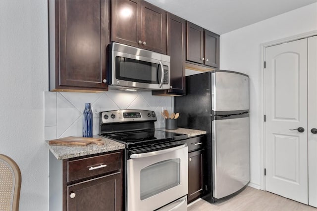 kitchen with appliances with stainless steel finishes, decorative backsplash, dark brown cabinets, light stone countertops, and light wood-style floors