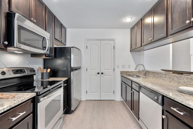 kitchen with appliances with stainless steel finishes, a sink, light wood-type flooring, dark brown cabinetry, and light stone counters