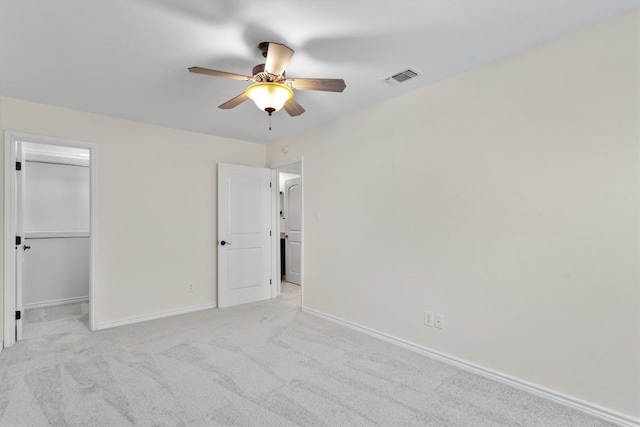 unfurnished bedroom with baseboards, a spacious closet, light carpet, a ceiling fan, and a closet