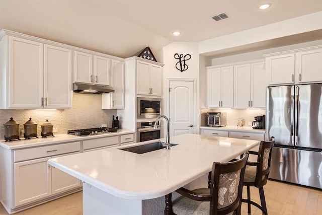 kitchen featuring a kitchen bar, appliances with stainless steel finishes, light countertops, and under cabinet range hood