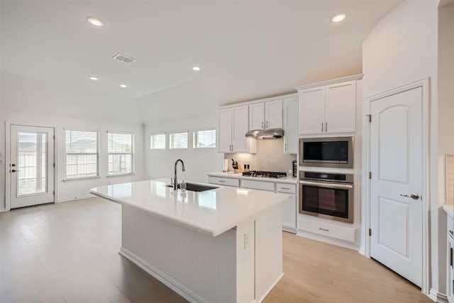 kitchen with under cabinet range hood, visible vents, a center island with sink, appliances with stainless steel finishes, and light wood finished floors