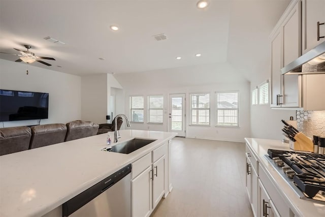 kitchen with a sink, light countertops, stainless steel appliances, open floor plan, and backsplash