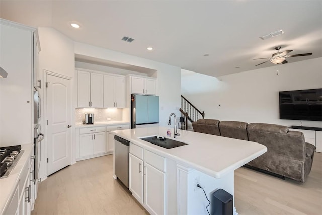 kitchen featuring a sink, open floor plan, ceiling fan, light wood finished floors, and stainless steel appliances