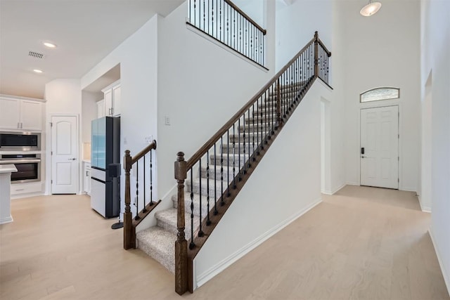 stairway with wood finished floors, a towering ceiling, baseboards, and recessed lighting