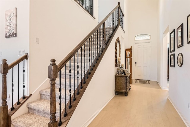 stairway with a towering ceiling, baseboards, and wood finished floors