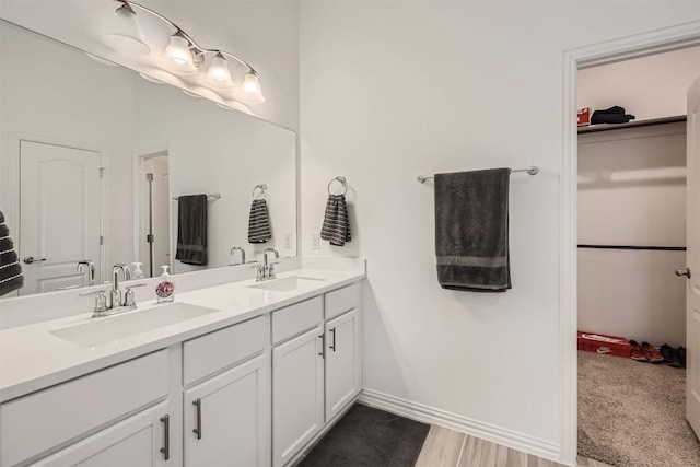 full bath featuring a sink, a walk in closet, baseboards, and double vanity