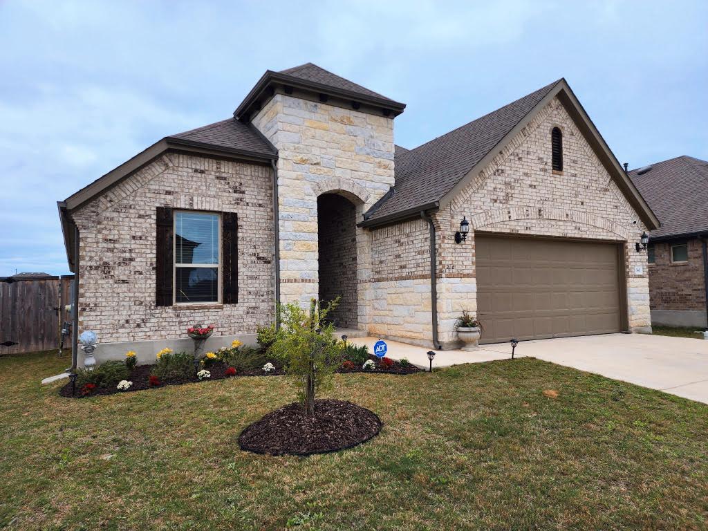 140 Periwinkle Ln, Bastrop, TX 78602 - french provincial home with driveway, a front lawn, stone siding, and an attached garage