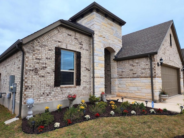 french country home with concrete driveway, roof with shingles, stone siding, brick siding, and a garage