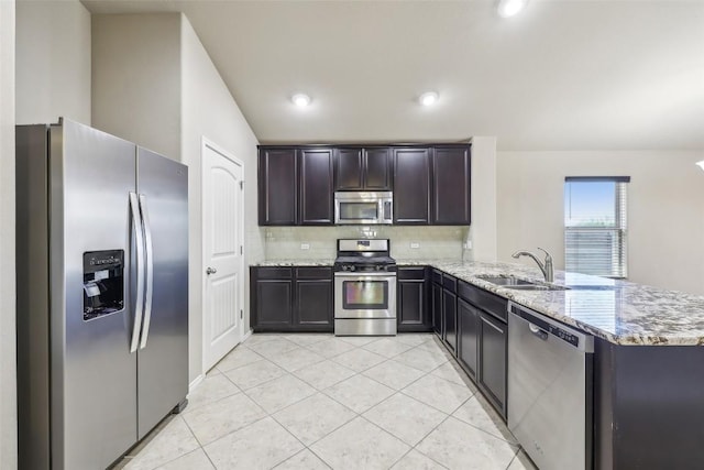 kitchen with backsplash, a sink, light stone counters, a peninsula, and stainless steel appliances