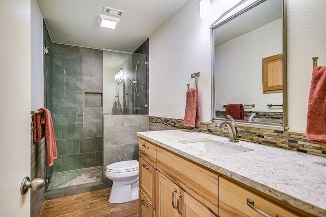 full bath featuring vanity, visible vents, wood finished floors, toilet, and tiled shower